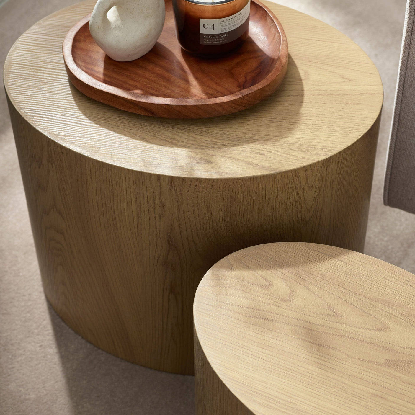 Close-up of light oak table tops showing wood grain, with a wooden tray holding a candle and small vase.