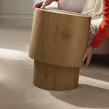 Person lifting the smaller light oak oval table, showing its smooth curved edges and natural wood grain.