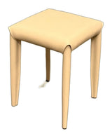 A modern square stool with a light beige upholstered seat and slim tapered legs, shown on a plain white background.