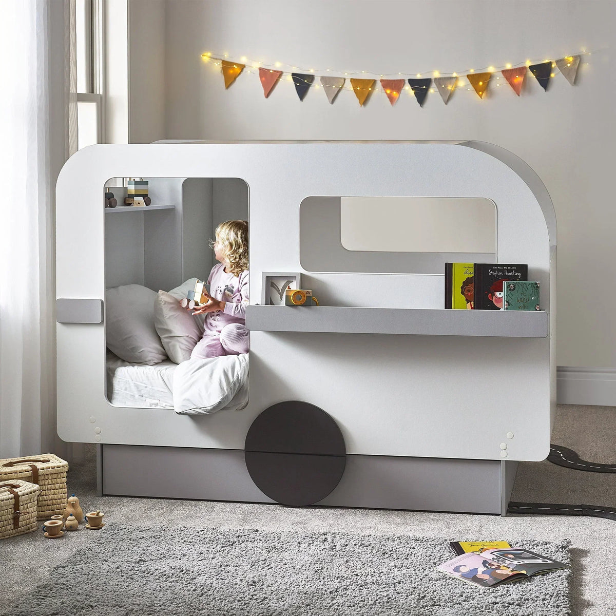 Children's caravan bed with window shelf, books, and bunting in cosy bedroom