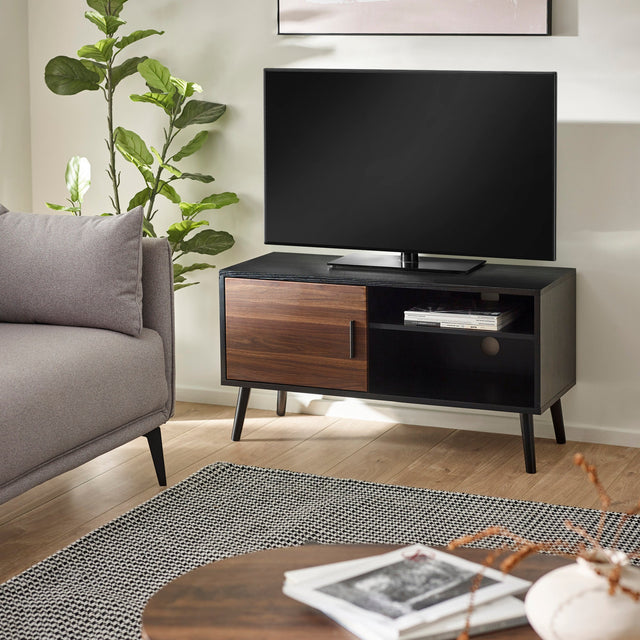 Small TV unit in black wood with one walnut door and open shelves, living room setting with gray sofa