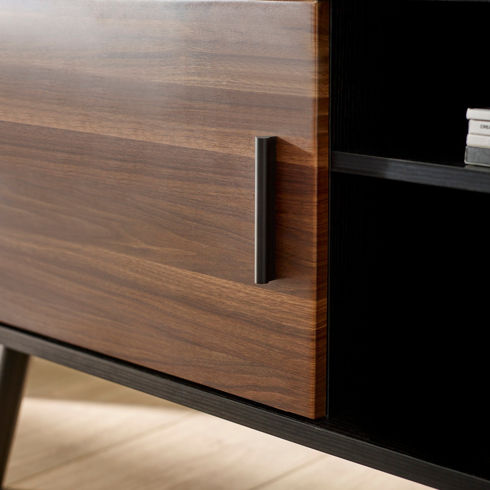 Close up of black metal handle on walnut door of the small TV unit