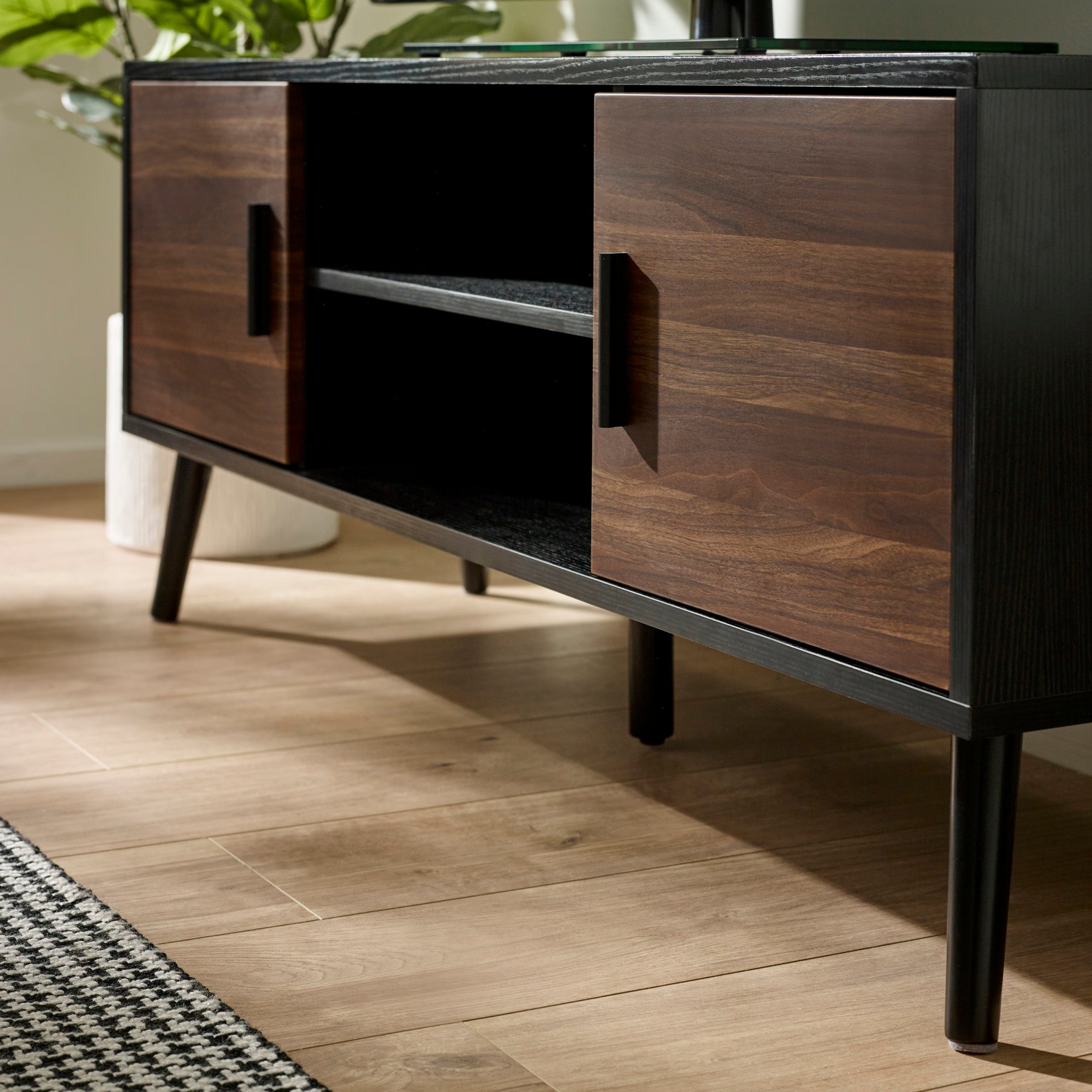 Angled view of TV unit with black frame, walnut wood cabinet doors, black handles, and black legs on wood floor