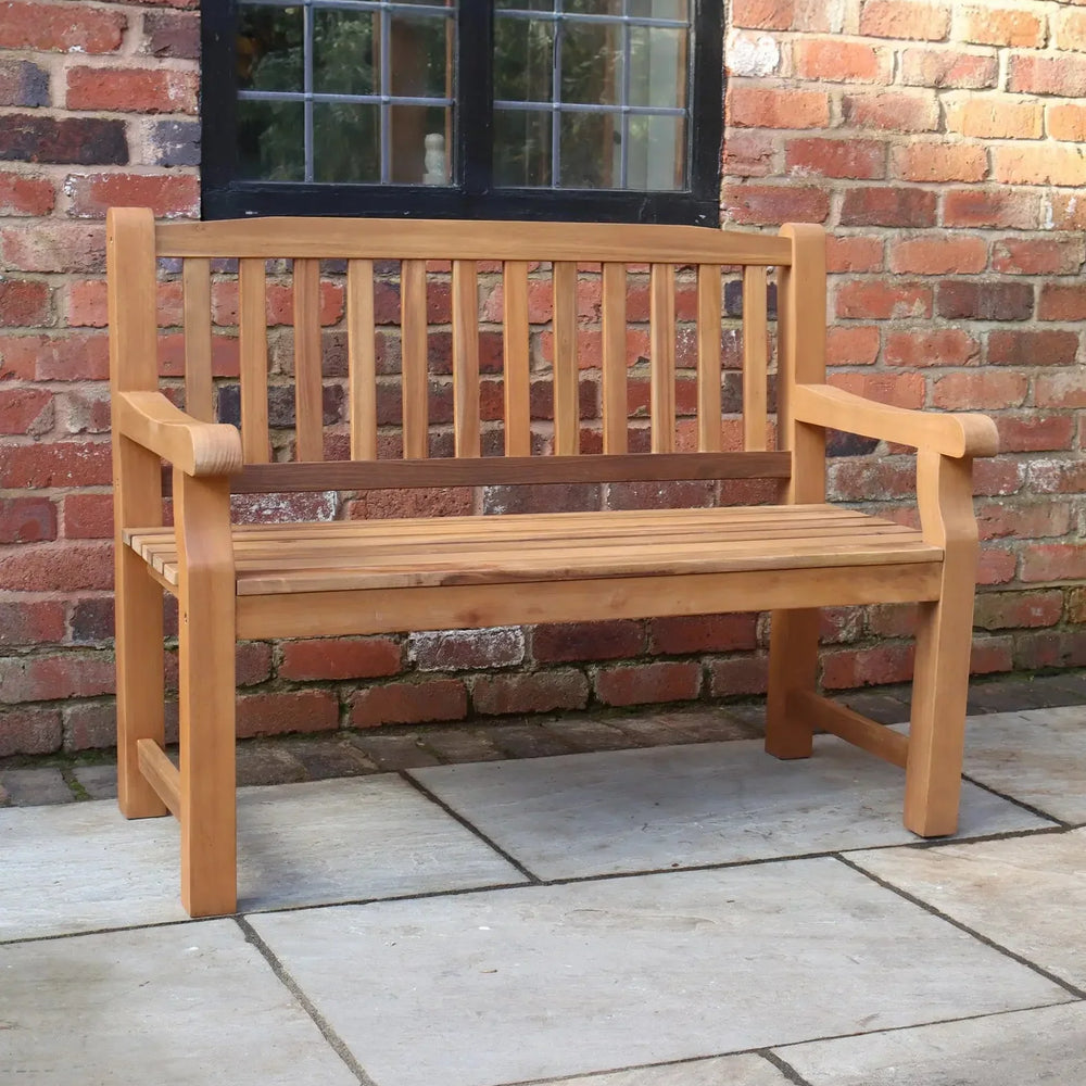 Wooden garden bench with slatted backrest on patio against red brick wall