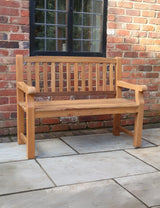 Wooden garden bench with slatted backrest on patio against red brick wall