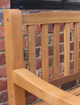 Teak wooden garden bench backrest and armrest detail against brick wall