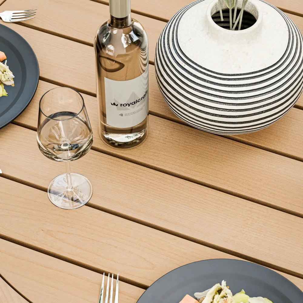 Wood effect outdoor dining table with plates, cutlery, glass, wine bottle and striped vase
