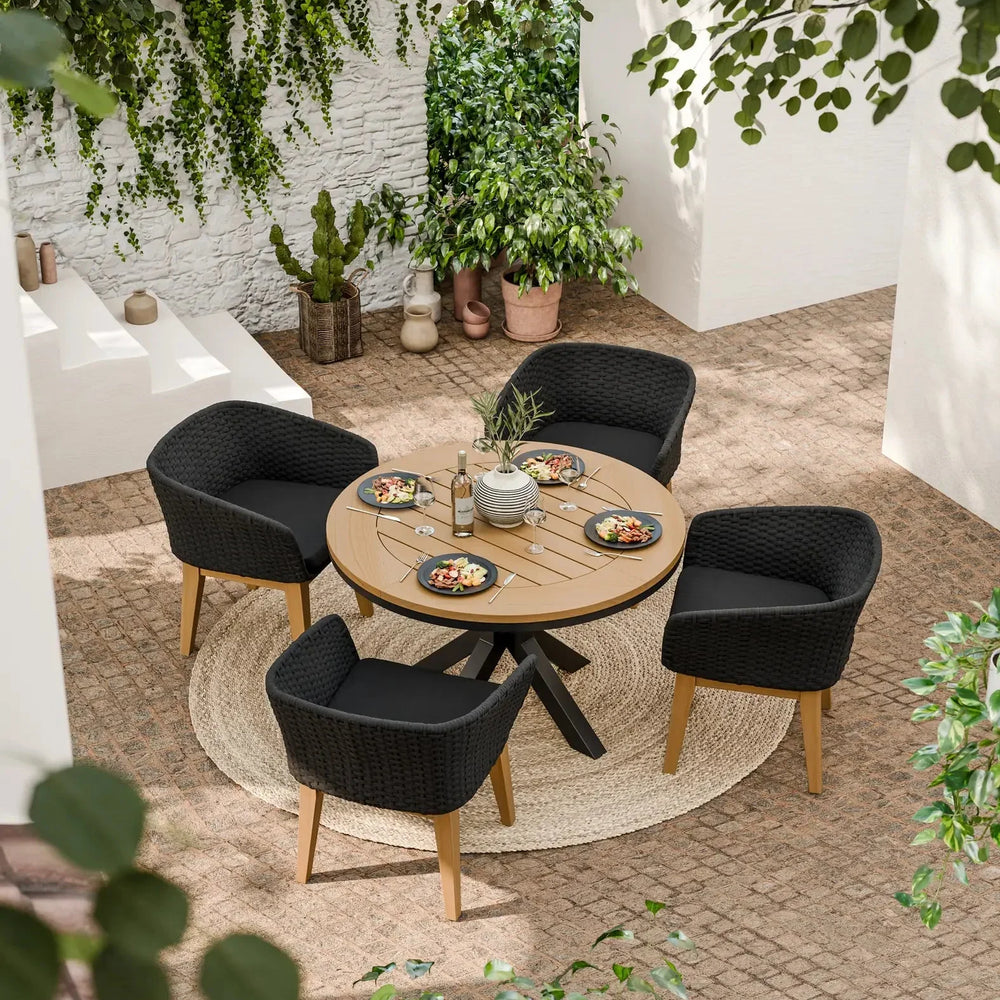 Round outdoor dining table with four black woven chairs on patio, set for lunch