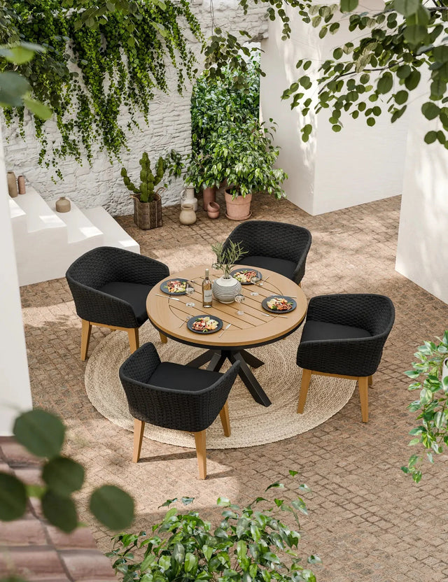 Round outdoor dining table with four black woven chairs on patio, set for lunch