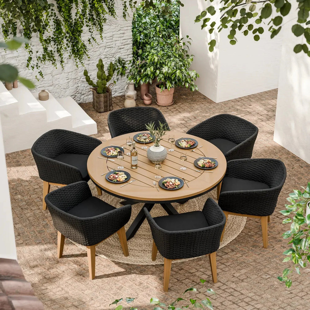 Round outdoor dining table with six black rattan chairs in a garden patio setting