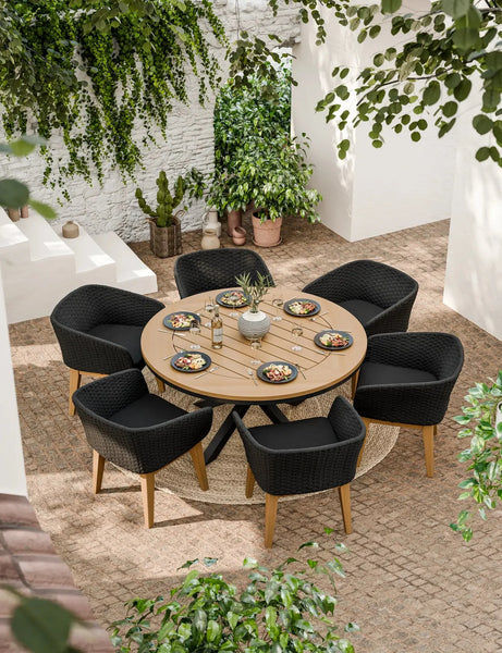 Round outdoor dining table with six black rattan chairs in a garden patio setting