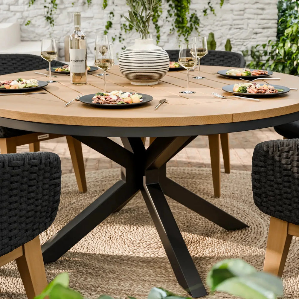 Round wooden dining table with black chairs, set for four, on outdoor patio