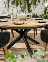 Round wooden dining table with black chairs, set for four, on outdoor patio