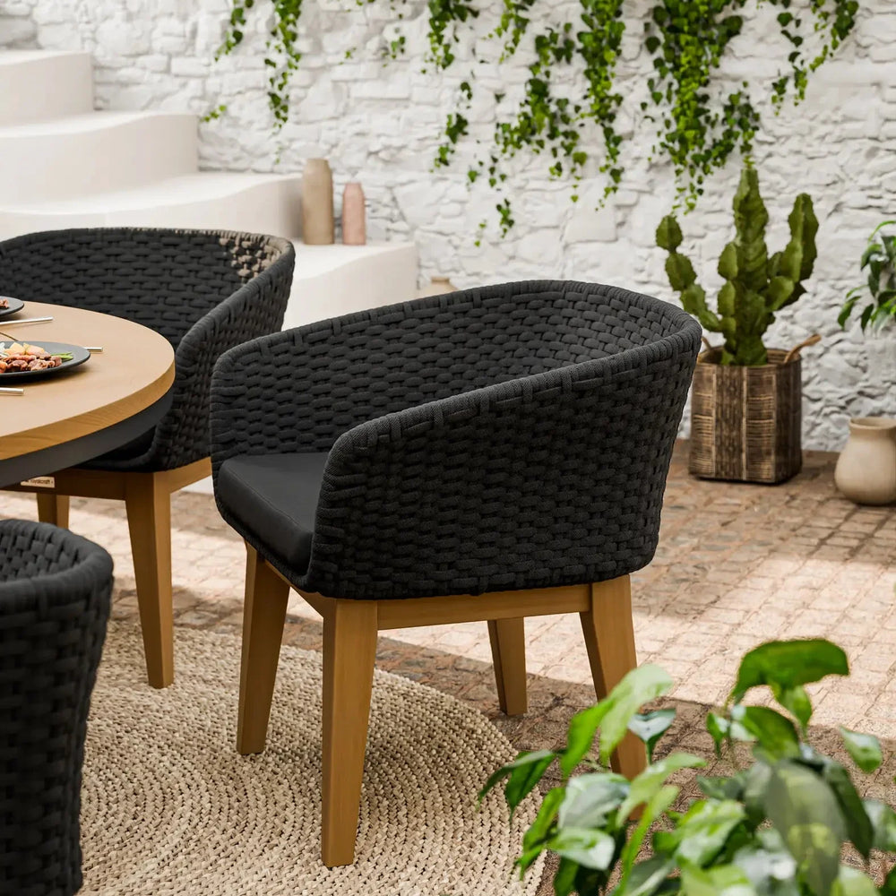 Black woven garden dining chair with cushion and wooden legs on patio near greenery