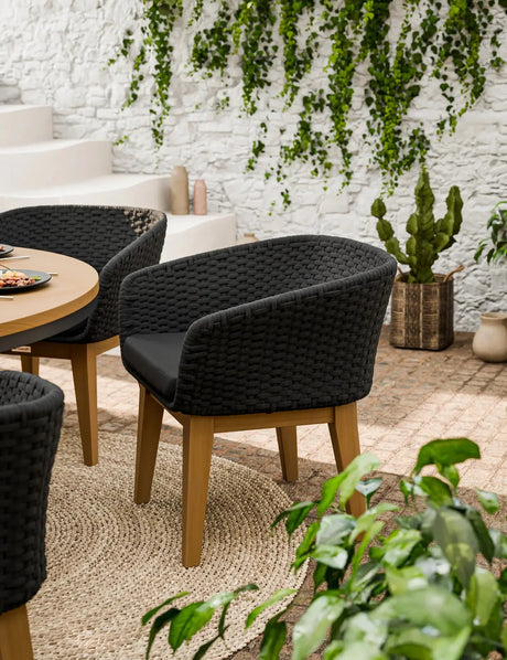 Black woven garden dining chair with cushion and wooden legs on patio near greenery