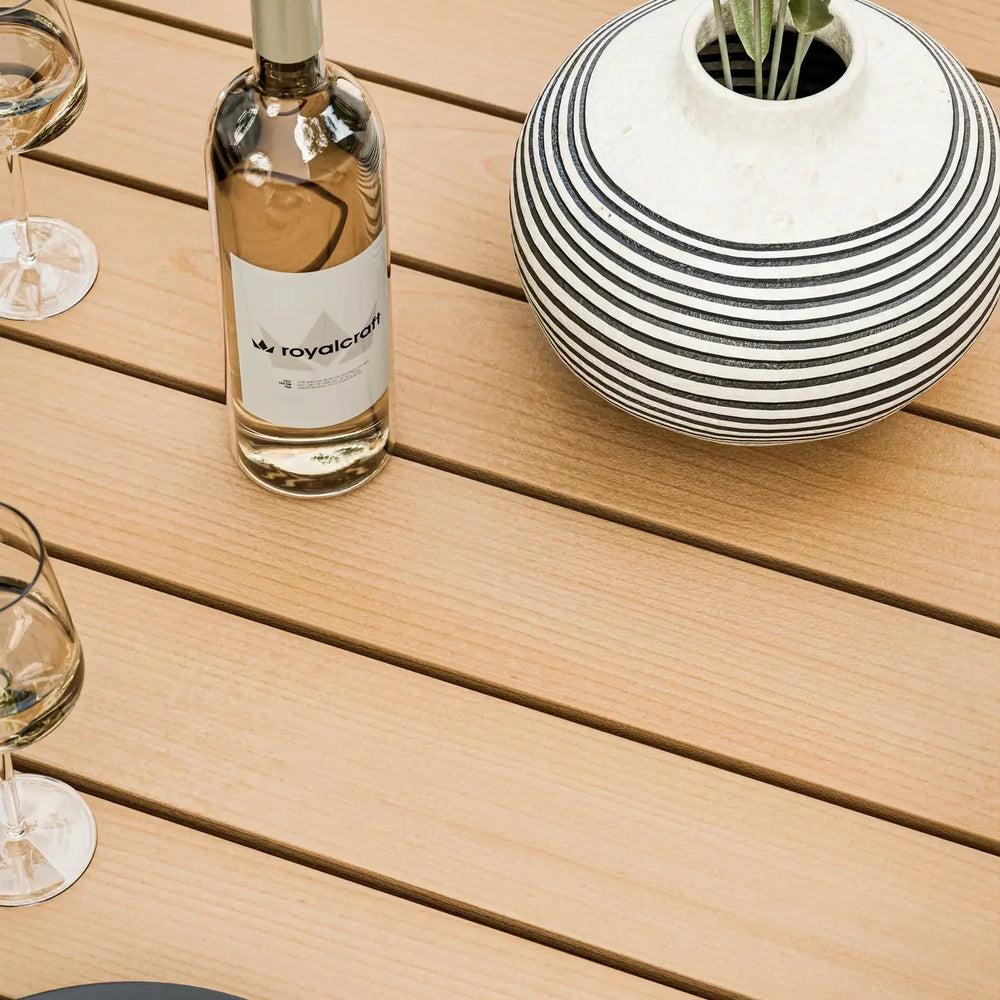 Wooden outdoor dining table with striped vase, wine bottle and glasses