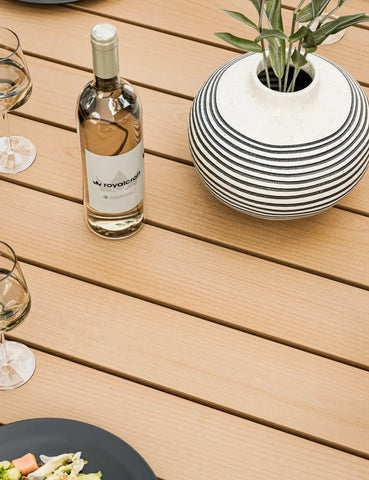 Wooden outdoor dining table with striped vase, wine bottle and glasses