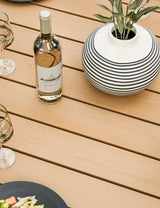 Wooden outdoor dining table with striped vase, wine bottle and glasses