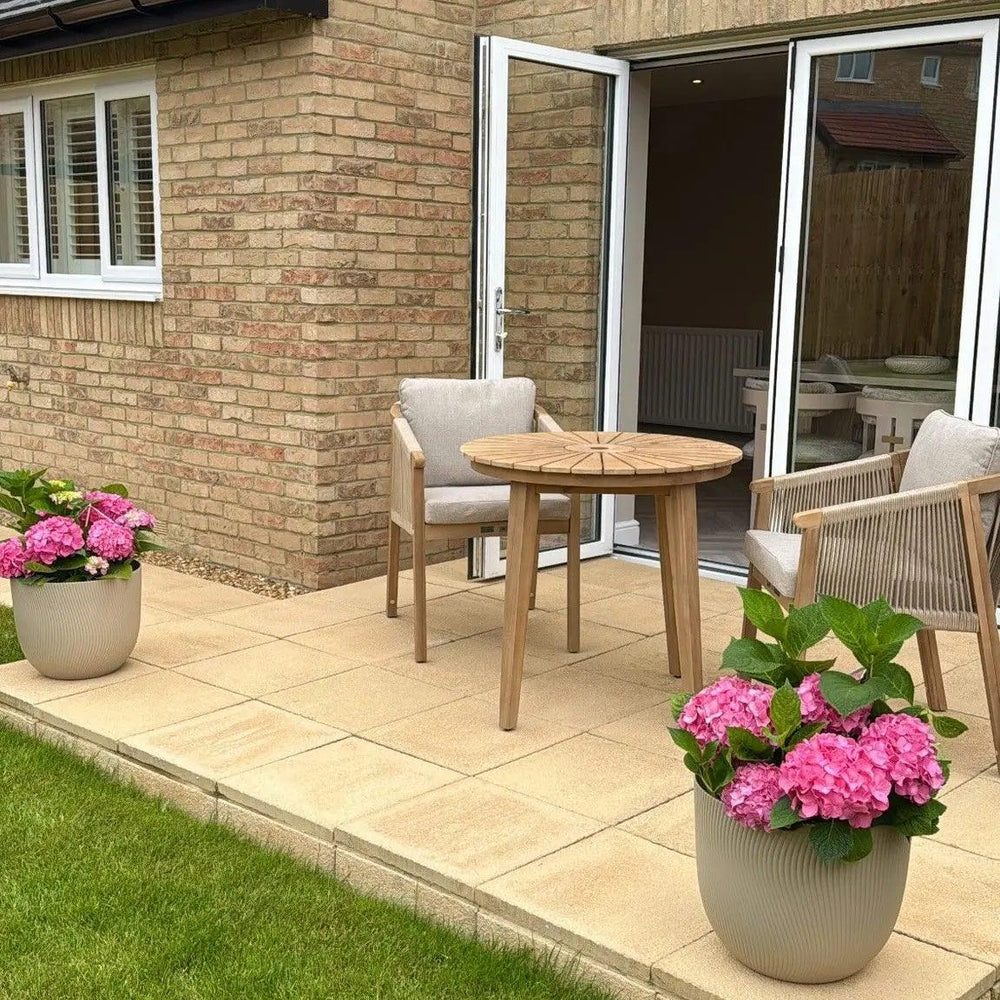 Wooden outdoor dining set with cushioned chairs on patio, flanked by pink hydrangea planters