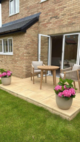Wooden outdoor dining set with cushioned chairs on patio, flanked by pink hydrangea planters