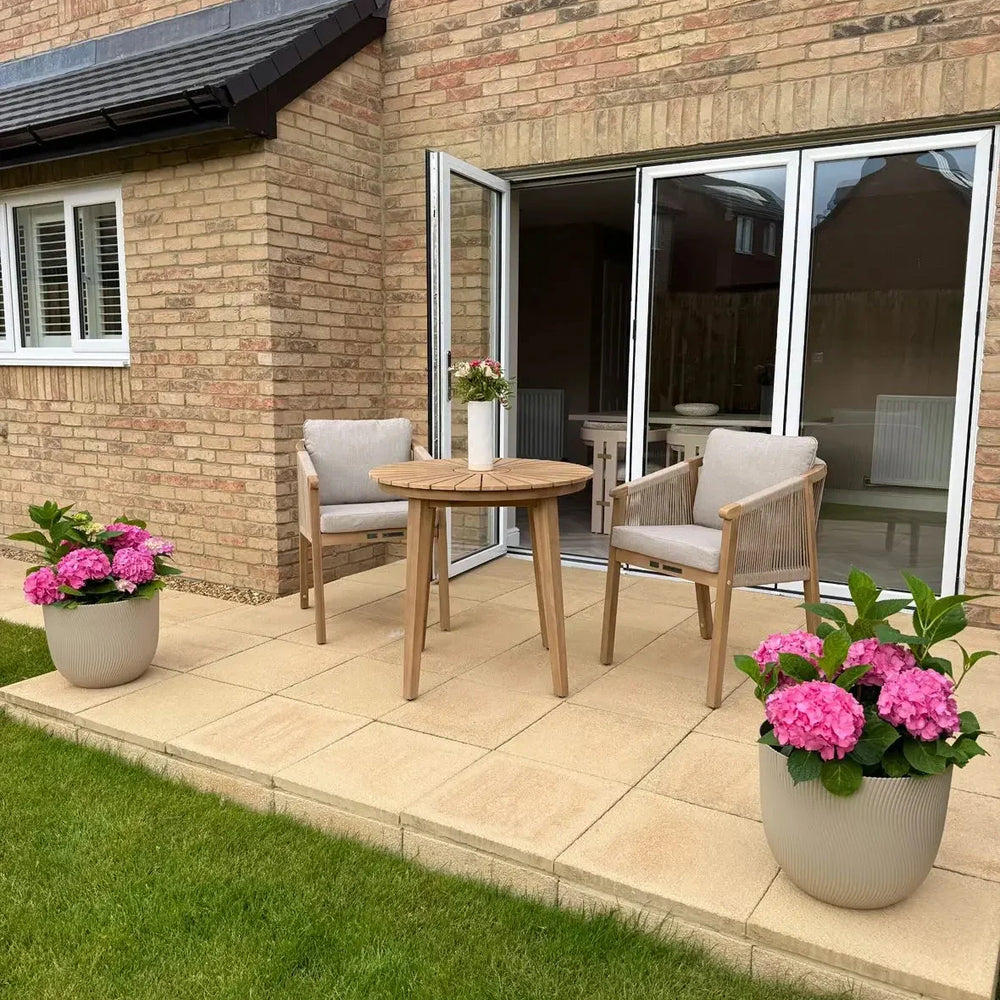 Outdoor patio set with wooden dining table, two chairs, and pink hydrangea planters