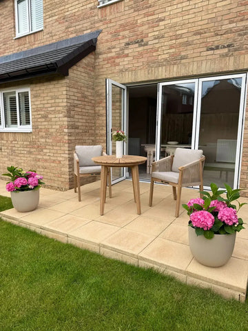 Outdoor patio set with wooden dining table, two chairs, and pink hydrangea planters