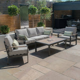 Grey outdoor sofa set with armchairs and coffee table on stone patio, garden backdrop