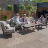 Grey outdoor sofa set with armchairs and coffee table on patio, people relaxing in sunlight