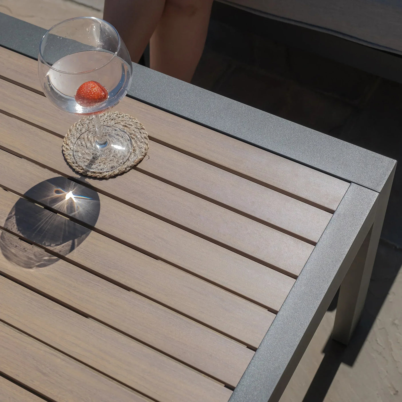 Slatted outdoor coffee table with metal frame, glass of water and strawberry on coaster