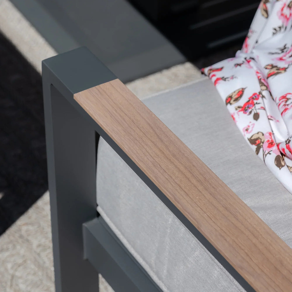 Grey outdoor sofa with wood effect armrest and light cushion, floral throw draped on seat