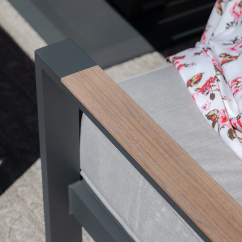 Grey outdoor sofa with wood effect armrest and light cushion, floral throw draped on seat