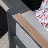 Grey outdoor sofa with wood effect armrest and light cushion, floral throw draped on seat