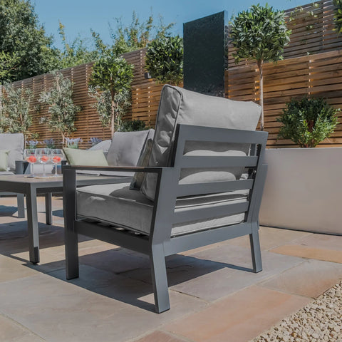 Grey outdoor garden chair with cushions on patio beside matching table and screen panel fence