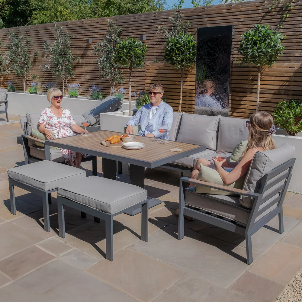 Grey outdoor garden sofa set with dining table, benches, and people relaxing on a patio