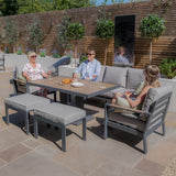 Grey outdoor garden sofa set with dining table, benches, and people relaxing on a patio