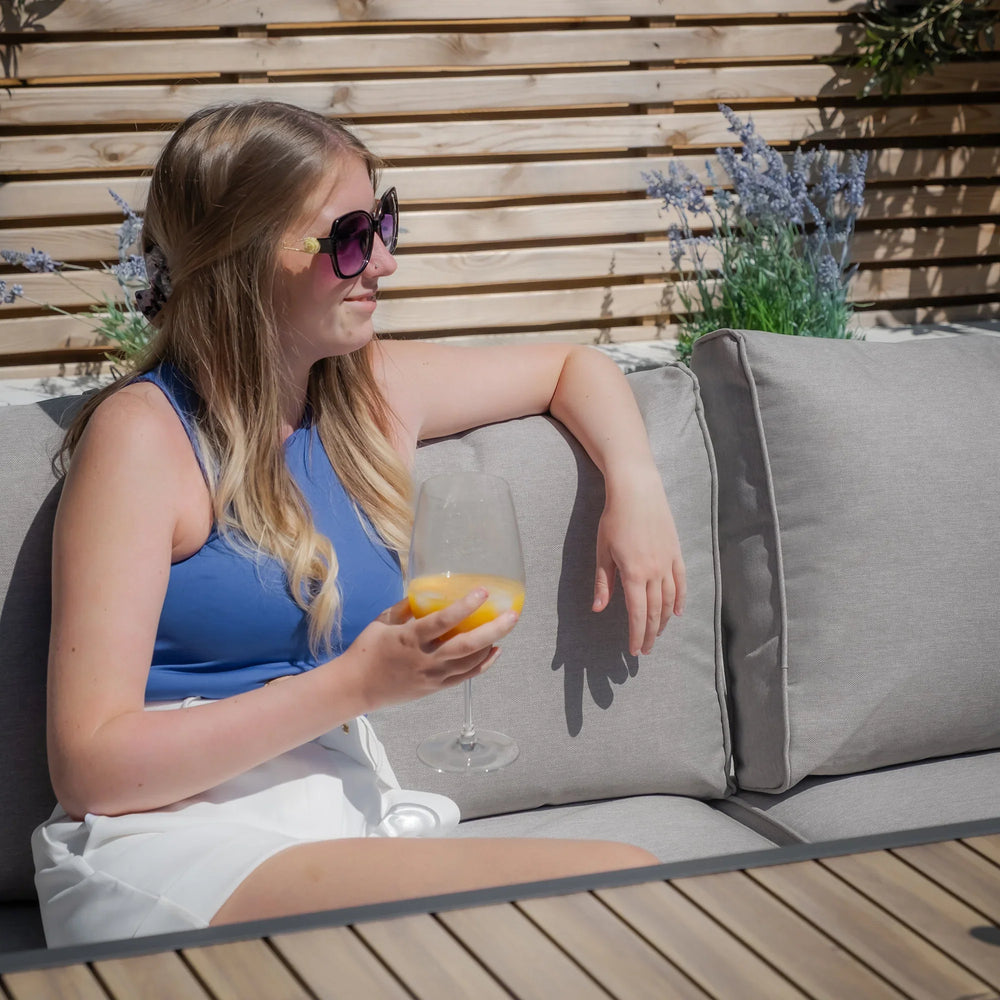 Grey outdoor sofa with cushions and woman relaxing in garden setting