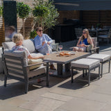 Grey outdoor garden furniture set with cushions and dining table on patio, people relaxing