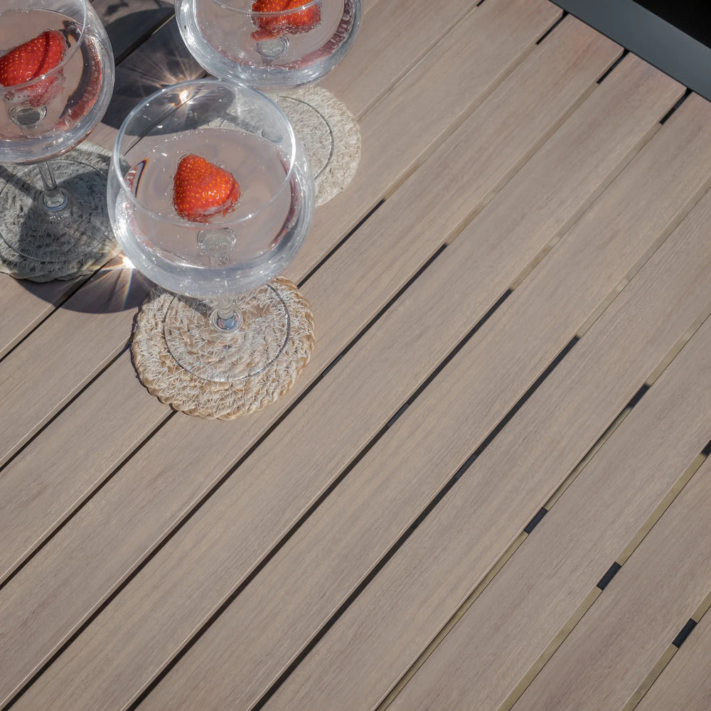 Slatted outdoor dining table in light wood finish with drinks served in glasses on coasters