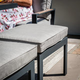 Grey outdoor ottoman with cushioned seat and black metal frame on patio