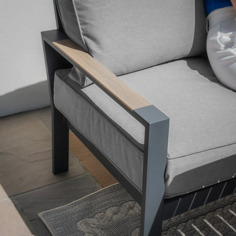 Grey outdoor sofa chair with metal frame, light wood armrest, and thick cushioned seat
