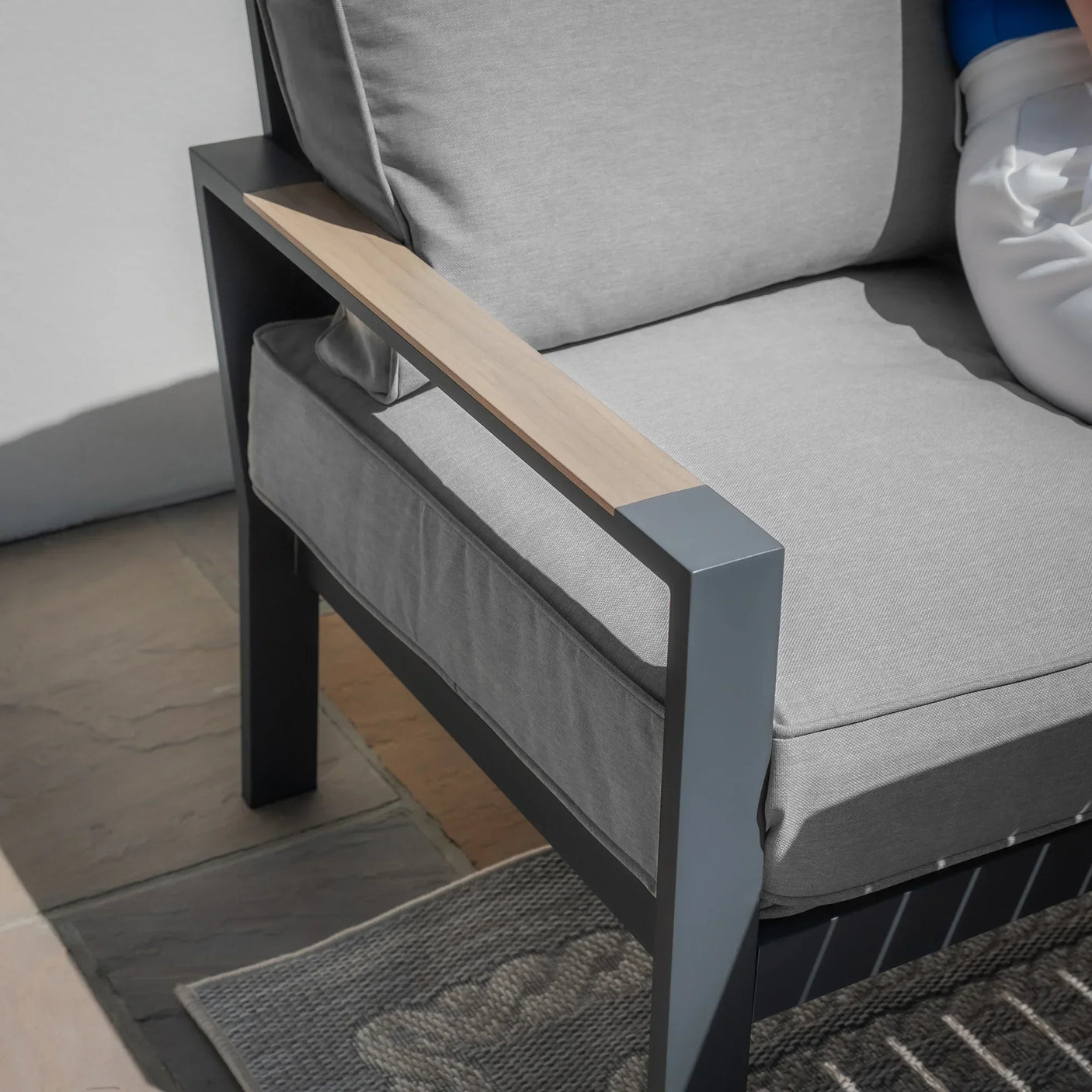 Grey outdoor sofa chair with metal frame, light wood armrest, and thick cushioned seat