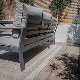 Grey outdoor sofa with metal frame and cushions on patio by wooden privacy fence