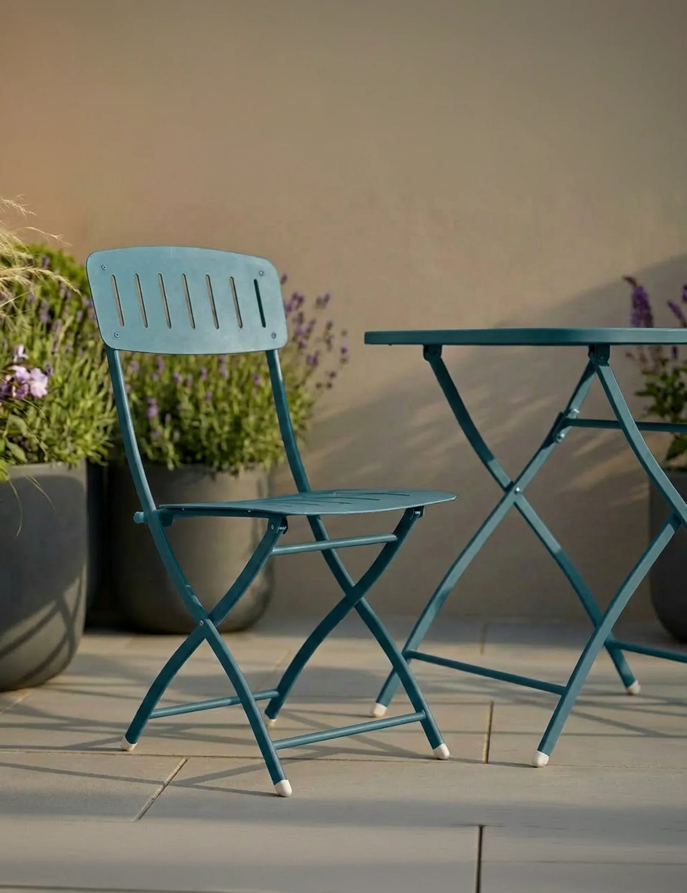 Teal metal garden chair and foldable table on patio with potted plants in background