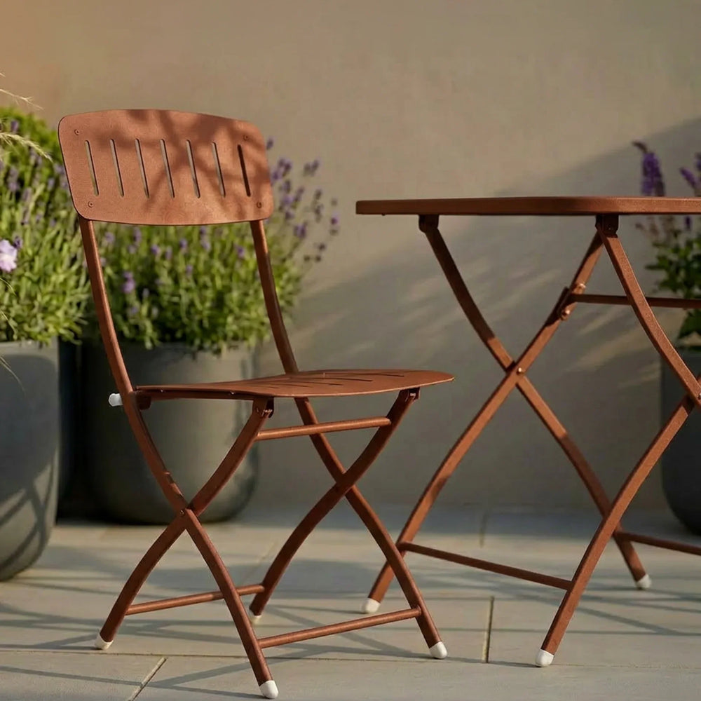 Brown folding garden chair and table set on patio with potted plants in background