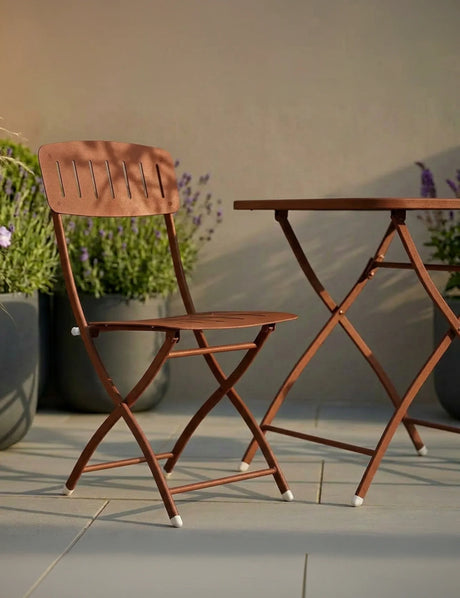 Brown folding garden chair and table set on patio with potted plants in background