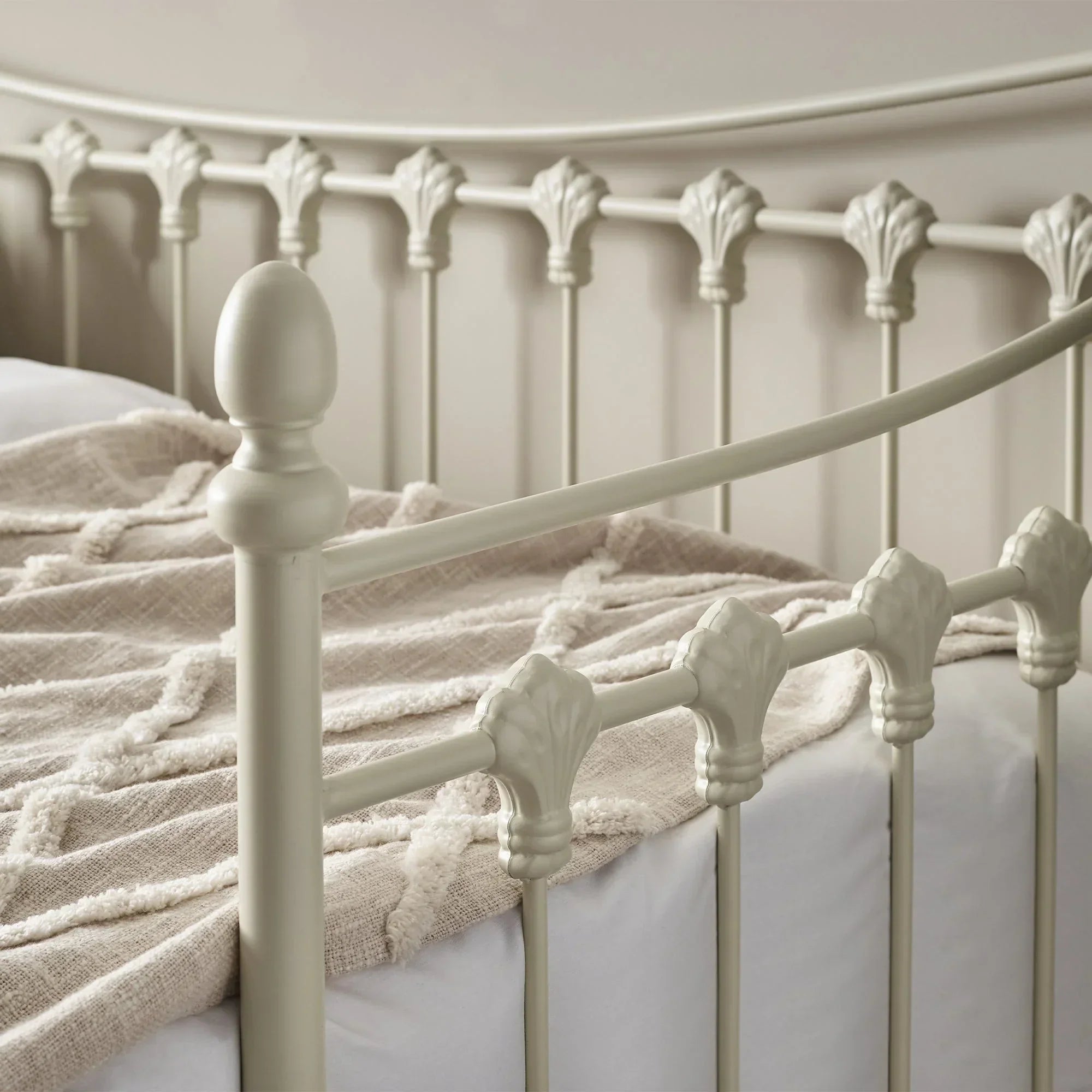 Stone white metal daybed with decorative spindle detail and curved frame, close-up view
