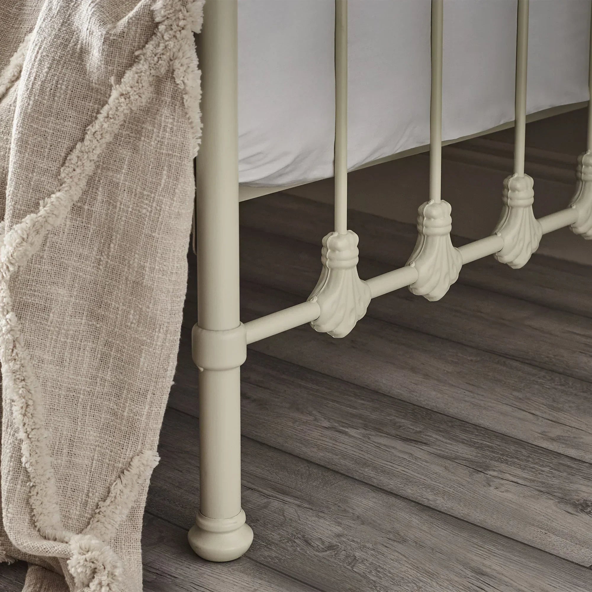 Stone white metal daybed frame with decorative finials and cream textured blanket draped