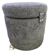 A round, upholstered storage ottoman or stool with a textured gray fabric cover, featuring a small side tab with gold-tone metal studs and a small gold tag near the base, shown on a plain white background.