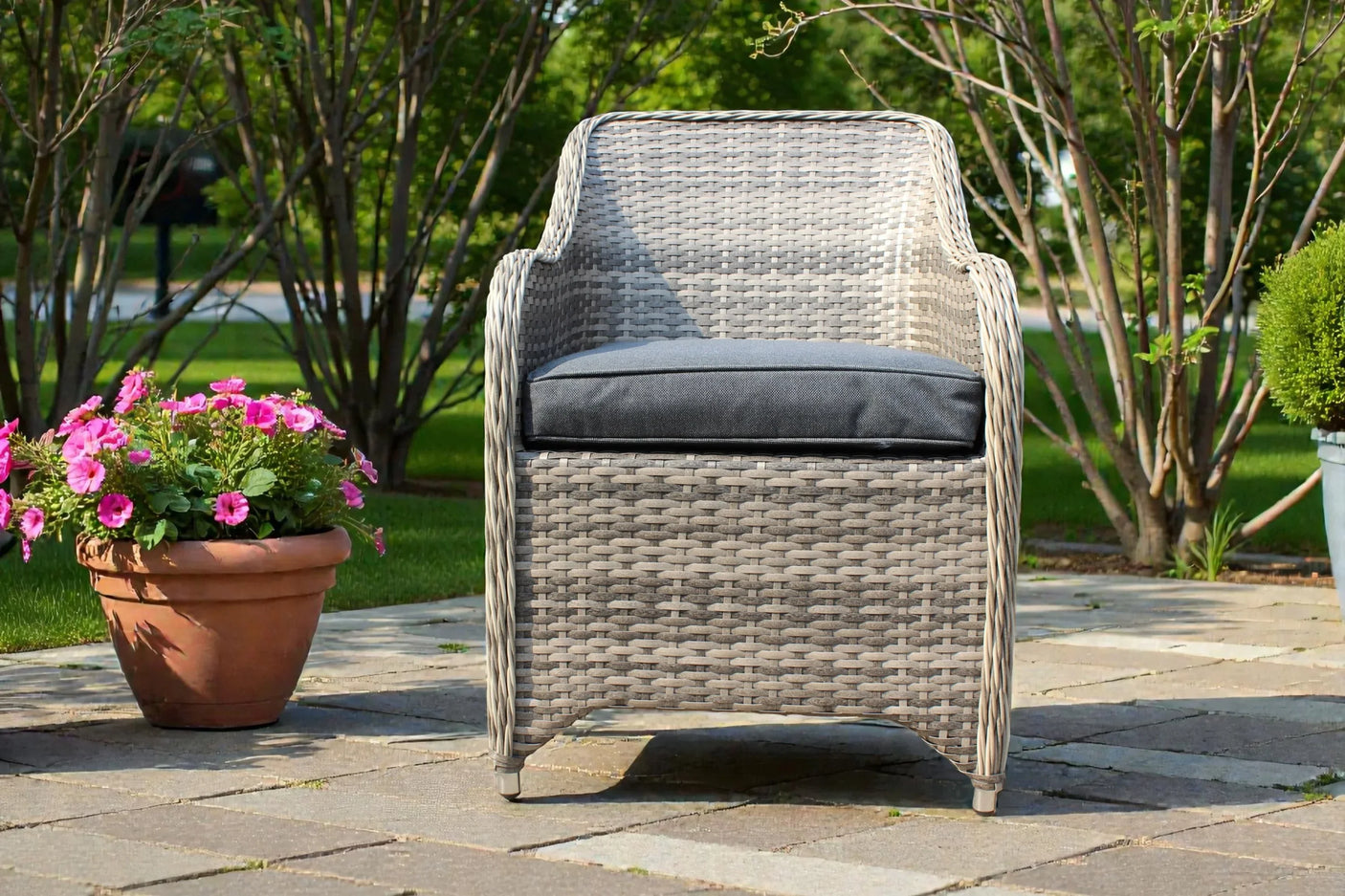 Grey rattan garden chair with dark cushion on patio, pink flowers in terracotta pot beside