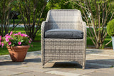 Grey rattan garden chair with dark cushion on patio, pink flowers in terracotta pot beside
